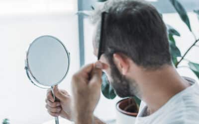 Ein Mann schaut sich im Spiegel an und macht sich Sorgen über Haarausfall.