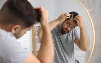 Mann untersucht seine Kopfhaut vor dem Spiegel